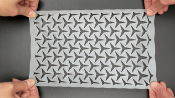 two sets of hands pull a perforated sheet taught across a gray surface