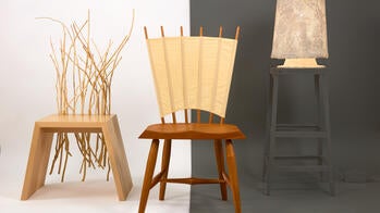 two sculptural wooden chairs and an end table stand left to right against a split white and dark gray background