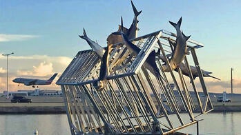 art installation on water featuring marlins and a house-shaped metal cage
