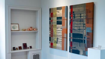 two sets of three-dimensional artworks sit on bookcase shelves, next to a pair of wall-mounted fabric paintings