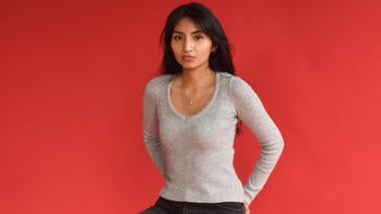 Gisela Ochoa MFA 28 GD seated on a stool against a bright red backdrop