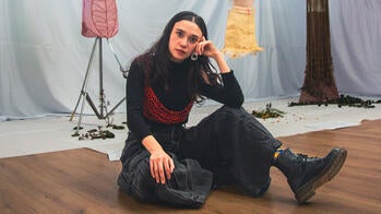Maria Gutierrez Hurtado MFA 28 TX seated in front of some of her textiles
