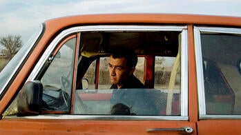 a man looking out the window of an old-fashioned orange sedan