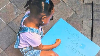 a young Black girl and a piece of paper that says Black kids matter