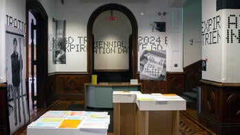 several exhibition podia display printed matter in a room with walls displaying the text "Triennial 2024 Expiration Date" in a dot-matrix typeface