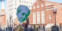 Small paper cutout of Helen Metcalf's head held up in front of RISD buildings