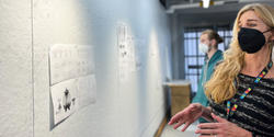 Faculty member Mary Jane Begin reviews student work pinned to wall