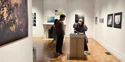 Visitors look through Ethan Brossard's photo book in the woods gerry-gallery on opening night of the 2023 photography triennial