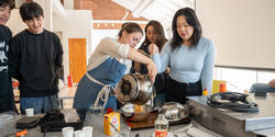 A group of students and a professor pour caramel into a steel bowl