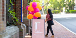 A person walks outside past a project open door sign