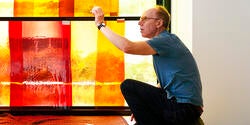 artist Spencer Finch kneels in front of a stained glass installation in progress