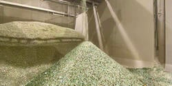 an industrial machine sprays shards of broken green glass into a huge pile