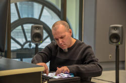 Shawn Greenlee operates a digital sound tool inside a room with speakers and a large window in the background