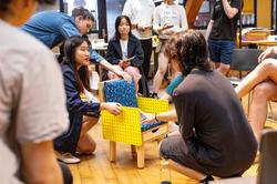 several students look at and discuss a small yellow chair during a studio critique