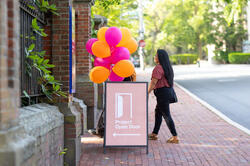A person walks outside past a project open door sign