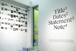 two gallery walls, with a series of black and white images on the left wall, and the words Title, Dates, Statement and Note on the right wall