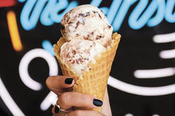 A person with black nail polish is holding an ice cream in a waffle cone