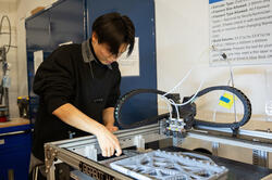 a student uses a putty knife to remove work from 3D printer
