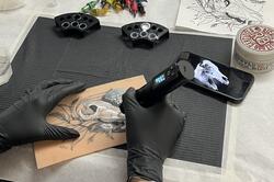 a person practices tattooing on fake skin with an image of a skull