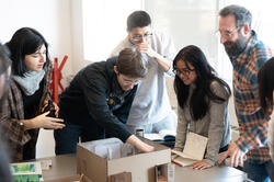 faculty member Adam Thabo and students gather around a model of the exhibition in progress