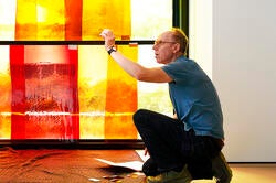 artist Spencer Finch kneels in front of a stained glass installation in progress