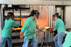 three students in aqua lab coats work together in the hot shop