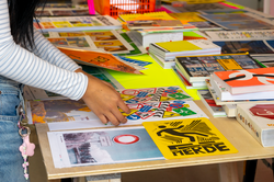 a student handles a multicolored print among several designed prints and books on a display table