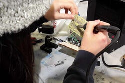 a pair of hands manipulating the wires on a circuit board at a workstation