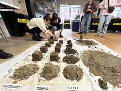 students stand around clay samples arranged on a workshop floor, with labels classifying the clay types as "compacted", "tamped" and "filled"
