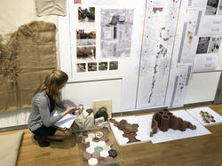 a student arranges multicolored hexagonal clay blocks in a pattern, in front of schematic illustrations pinned on a wall
