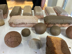 numerous clay objects on a table, including a layered brick and many molded clay spheres in shades of brown