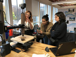 three people talk while observing a 3d printer extruding clay onto a flat surface