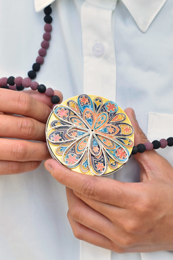 A person in a white shirt is wearing a colorful patterned necklace on a beaded thread.