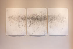 three pieces of paper with scattered black paint marks tacked up on a white wall