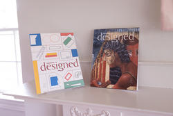 two issues of a magazine titled "designed" facing one another atop a mantel
