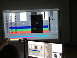a hand reaches up toward a computer monitor in a dark room, with the monitor displaying color bars and the number 36 repeated many times
