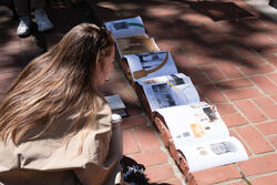 a student looks at a long unfolded piece of paper sitting on a brick step