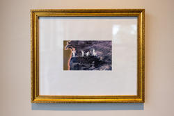 image of four person-shaped white figures walking on a landscape, mounted on a white surface inside a gold frame