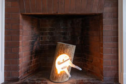 a log attached to a light-emanating sculpture stands upright inside a fireplace