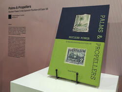 a black-and-green book titled Palms & Propellers sits atop a white display stand
