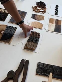 a hand reaches toward one of many rectangular-cut wood samples, colored several shades of brown