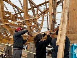 three students work outdoors on constructing a wooden boat