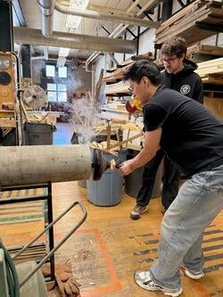 two students in a studio work on a large cylindrical wood structure