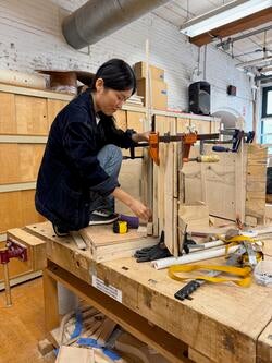 a student perched atop a woodshop workstation adjusts a vise