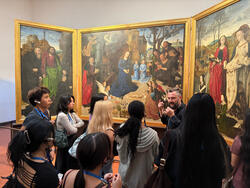 Students hear from a professor as they stand in front of a large painting