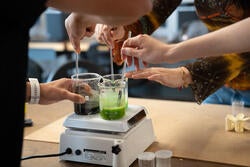 hands of several people stir colored fluids using lab equipment