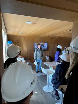 several people wearing hardhats stand in a room with wood-constructed walls and ceiling