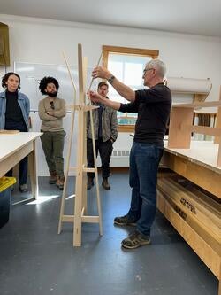 people discuss a tall wooden structure inside a workroom