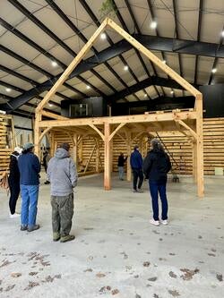 several people inside a shed look at simple wood frame in the shape of a tiny home