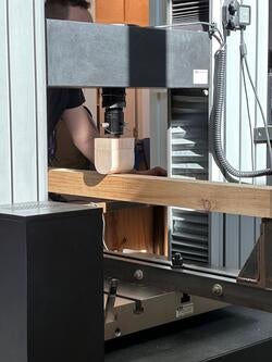 a person runs a wood beam through a strength-testing machine
